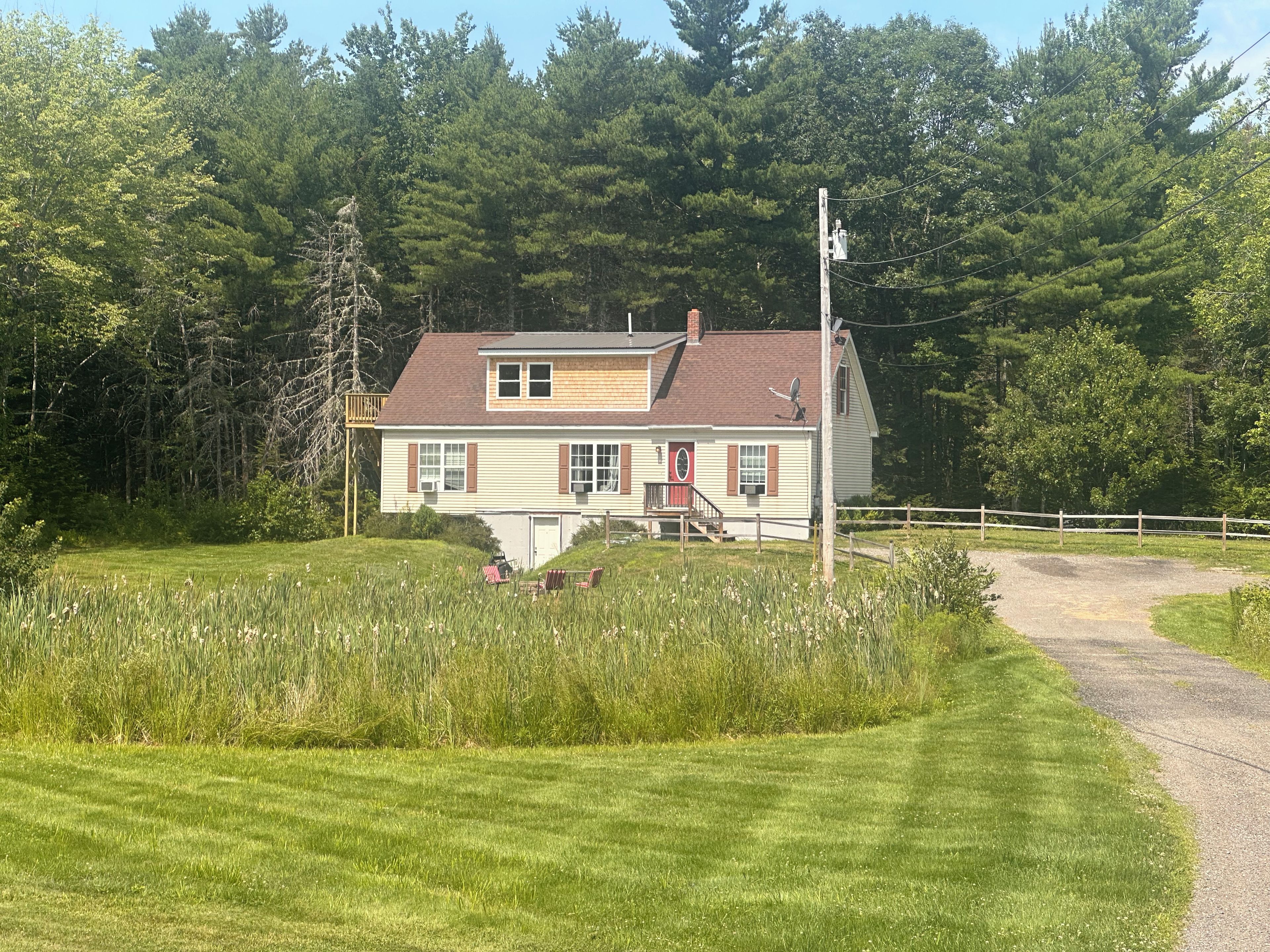 Une maison à deux étages avec une porte rouge et des volets marron, entourée d’une clôture en bois et bordée d’un chemin de gravier.