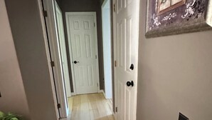 Un couloir doté d’un plancher en bois, de portes blanches et d’un luminaire au plafond.