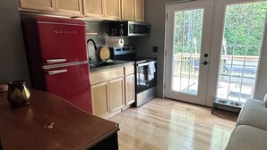Une cuisine avec des meubles de rangement en bois, un réfrigérateur rouge, un four à micro-ondes et un ventilateur de plafond.