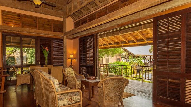 A spacious room with wicker furniture, large windows, and a view of greenery.