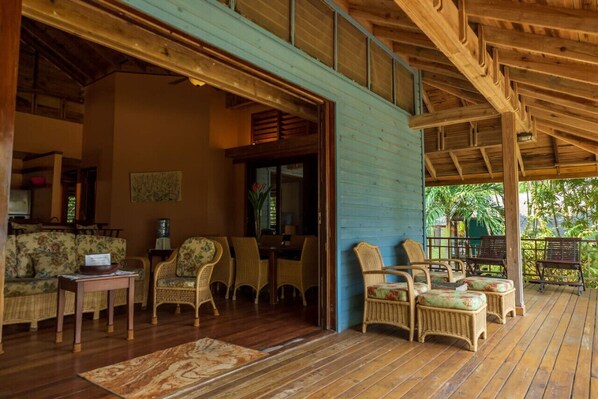 A wooden deck with wicker furniture, a dining area, and a view of greenery.