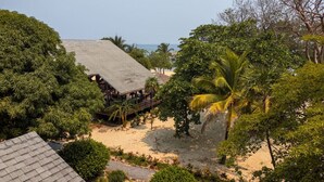 A beachside property with a wooden deck overlooking the sand and ocean, surrounded by lush greenery.