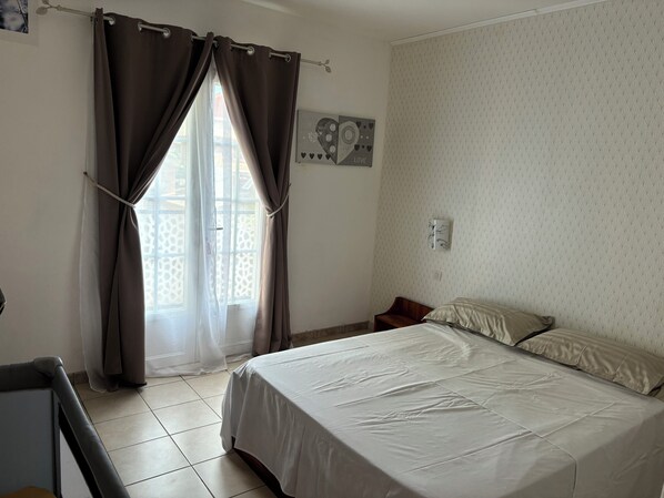 A bedroom with a bed, curtains, a wall clock, and a window with a view of a fence.