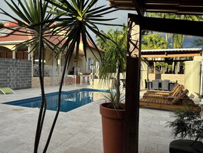 A pool area with a tiled deck, a large potted plant, and outdoor furniture.