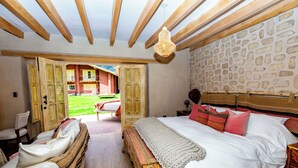 Een slaapkamer met een groot bed, houten balken, een stenen muur en een open deur naar een balkon.