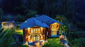 Een huis met twee verdiepingen, een balkon en een veranda, omringd door een tuin en bomen.