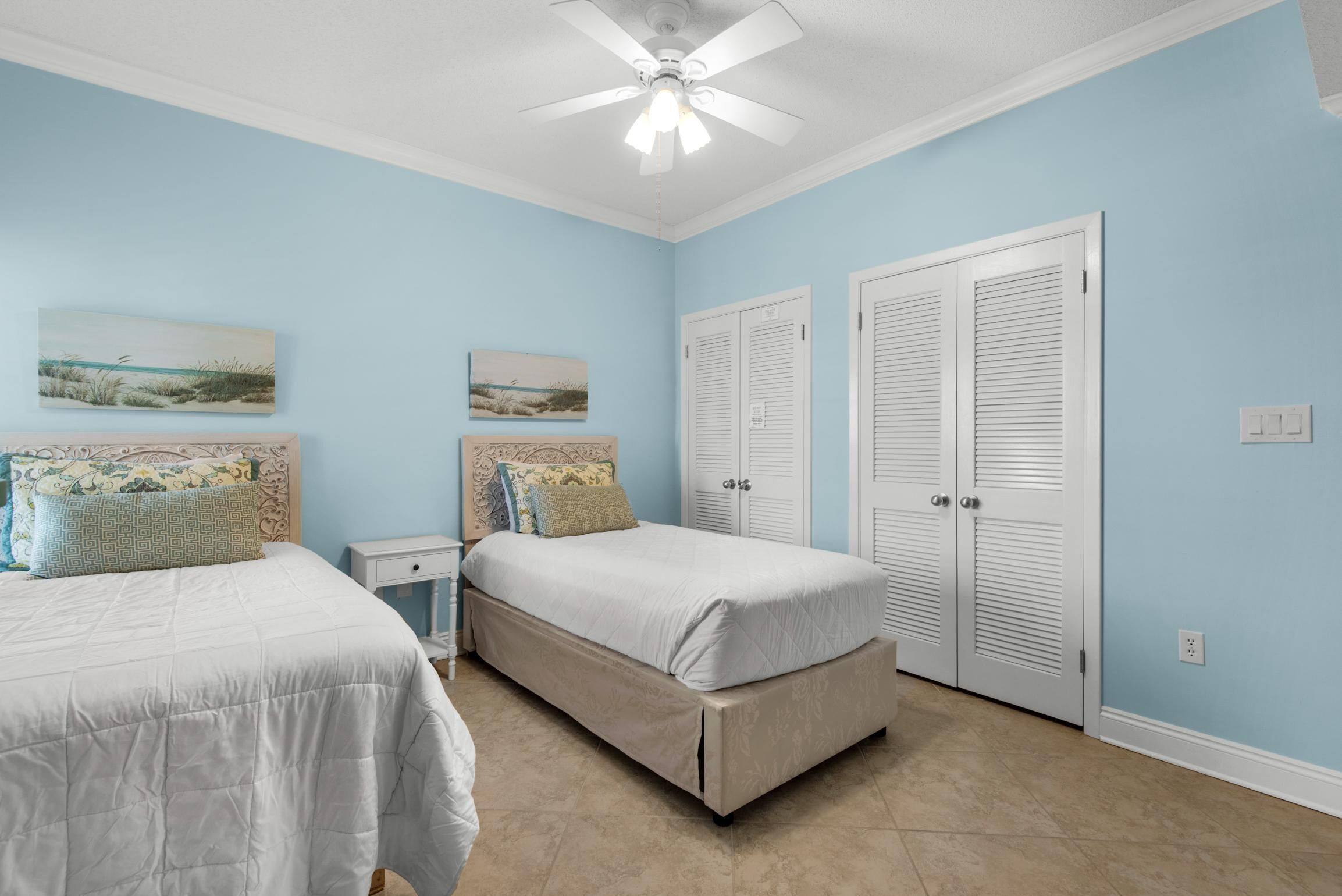 A bedroom with two beds, a nightstand, a ceiling fan, and two doors.