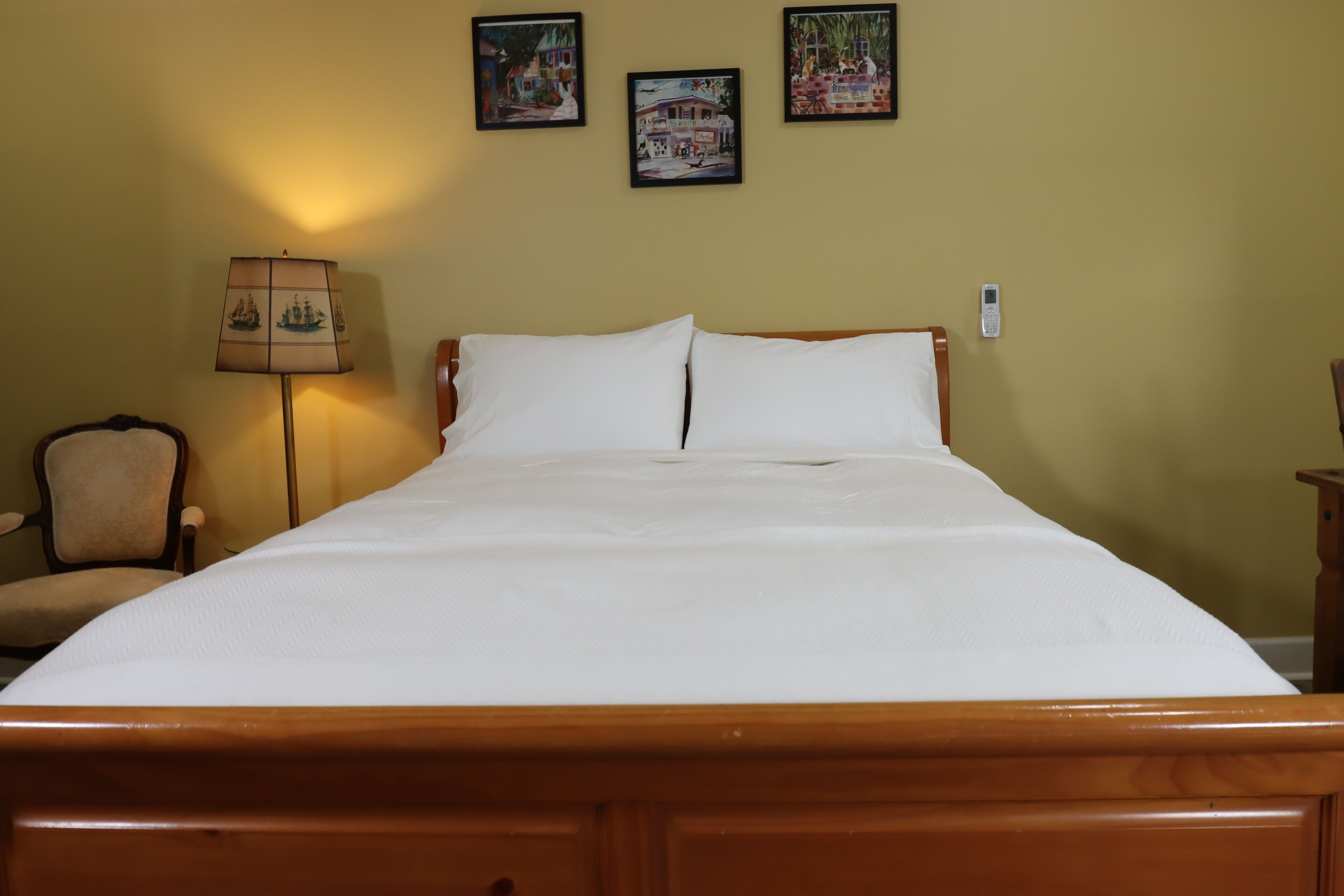 Una cama con sábanas blancas impecables en una habitación con cabecera de madera. Hay tres cuadros enmarcados en la pared sobre la cama.