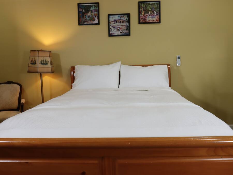 Een net opgemaakt bed met witte lakens in een kamer met een houten hoofdeinde. Boven het bed hangen drie ingekaderde foto’s aan de muur.