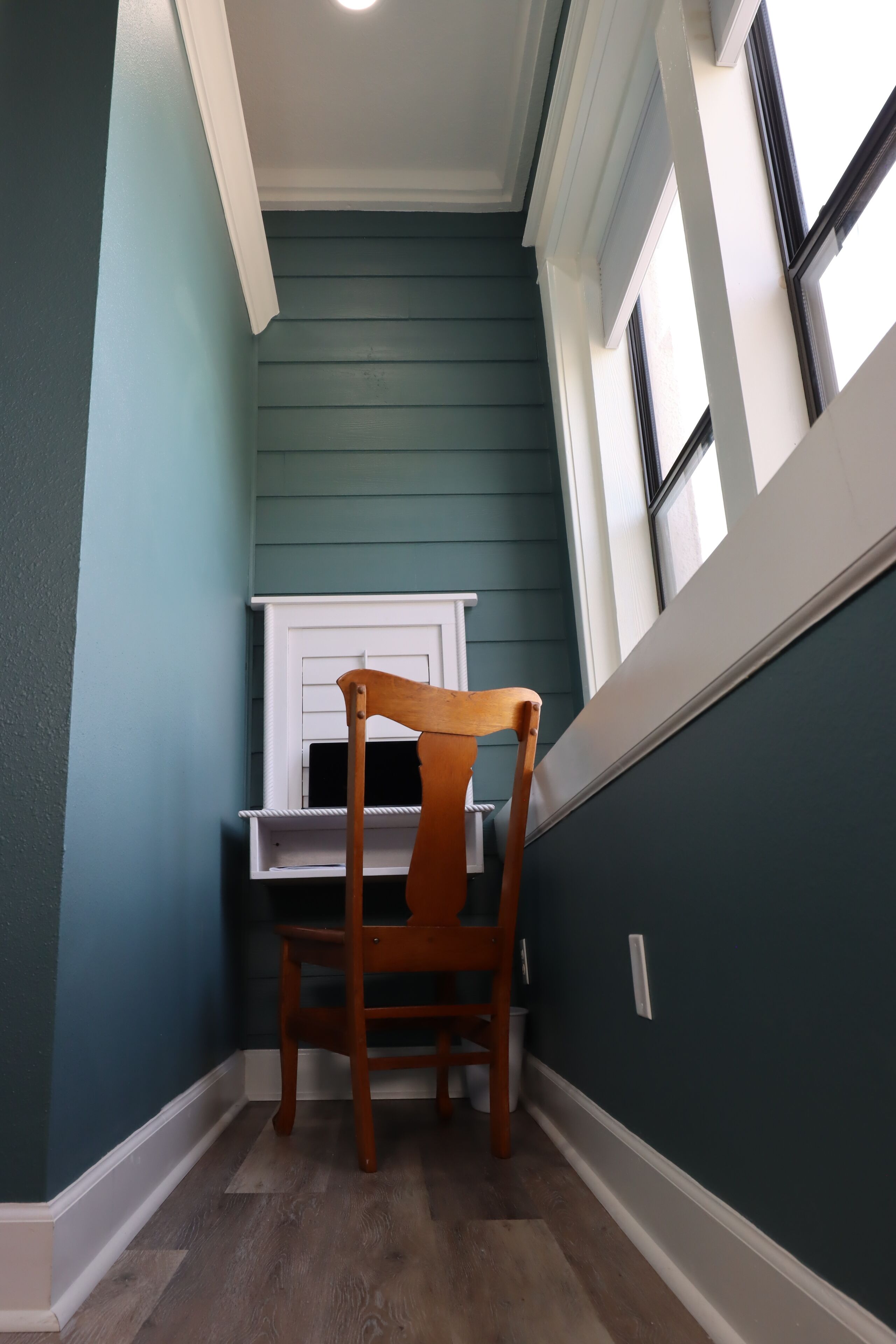 Une pièce d’angle avec une chaise en bois, une cheminée blanche et une fenêtre avec des stores.