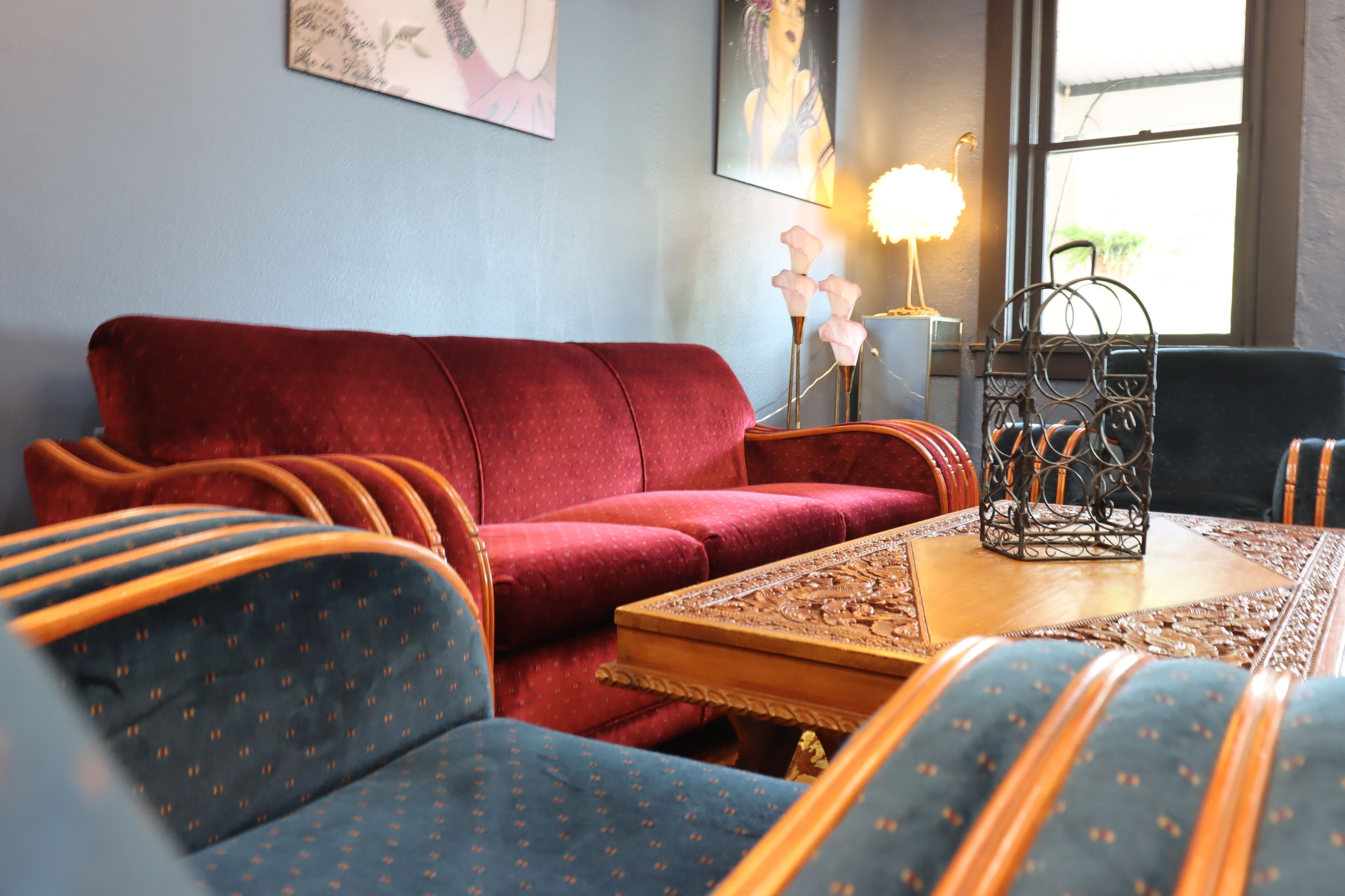 A living room with a red sofa, blue patterned chairs, a wooden coffee table, and a decorative metal lamp.
