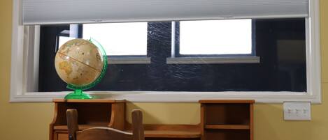 A classroom with a globe on a desk, a chair, and a window with blinds.