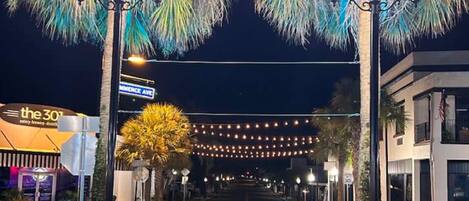A street at night with street lamps, palm trees, and a building with a sign that reads "the 30".