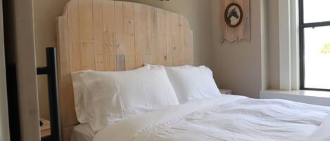 A neatly made bed with a wooden headboard, a wall-mounted coat rack, and a framed picture.