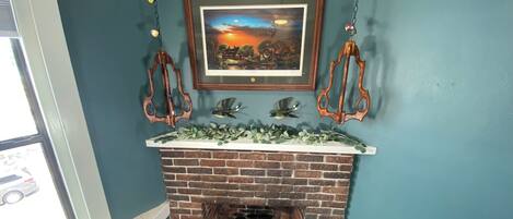 A brick fireplace with a framed landscape painting above it.