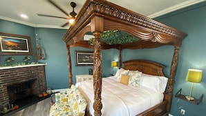 A four-poster canopy bed with a wooden frame, a brick fireplace, and a bench with a floral cushion. - The Roanoke Hotel (Sebring)