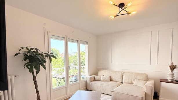 A modern living room with a sofa, ottomans, a coffee table, a potted plant, and a ceiling light fixture.