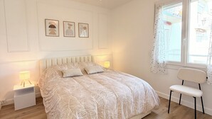 A bedroom with a bed, bedside tables, a chair, a window with curtains, and wall-mounted artwork.
