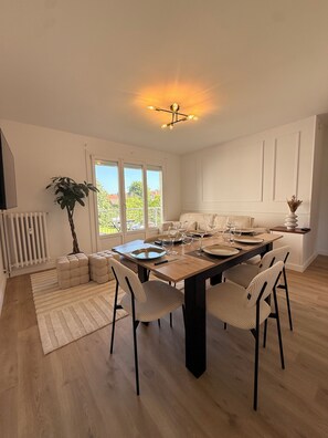 Un coin repas avec une table en bois, dressée pour quatre personnes, entourée de chaises, d’une plante en pot et d’un radiateur.
