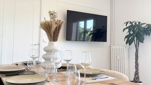 A dining area with a wooden table set for four, a white vase with dried plants, a potted plant, and a TV mounted on the wall.
