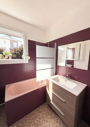 Un baño con bañera, tocador, espejo y ventana.