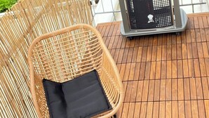 En træterrasse med en fletstol og et bord, grill og et hus i baggrunden.