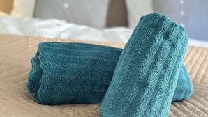 En pænt redt seng med et beige quilt og to sammenfoldede turkise håndklæder ovenpå.