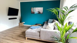 En moderne stue med en væg i teal farve, en grå sofa og en stor plante.