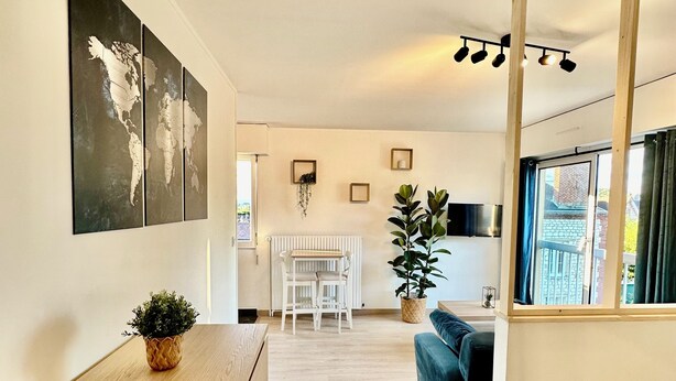 Une pièce moderne et bien éclairée, avec un bureau en bois, un canapé confortable, un grand miroir et une vue sur l’extérieur par une fenêtre.