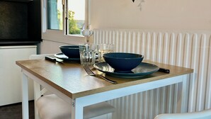 Un coin repas avec une table en bois, des chaises blanches, un saladier, des verres et une plante suspendue.