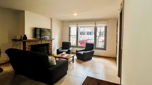 A living room with a fireplace, two armchairs, a coffee table, and a TV on a stand. - RentUp- Casa a pasos del Centro Cívico (San Carlos de Bariloche)