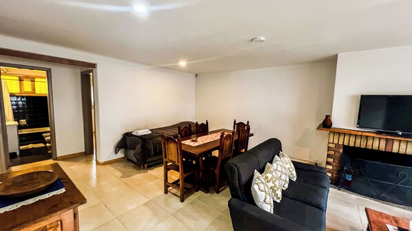 Una sala de estar con un sofá, una mesa de comedor con sillas, un televisor sobre un mueble bajo y una chimenea.