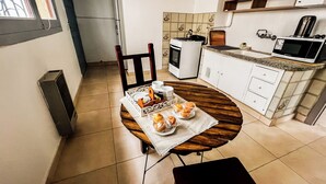 A compact kitchen with white cabinets, a microwave, and a stove. There's a dining table with a placemat and a tray of pastries. - RentUp- Casa a pasos del Centro Cívico (San Carlos de Bariloche)