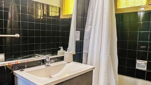 A bathroom with a white sink, dark tiled walls, a bathtub, and a shower curtain. - RentUp- Casa a pasos del Centro Cívico (San Carlos de Bariloche)