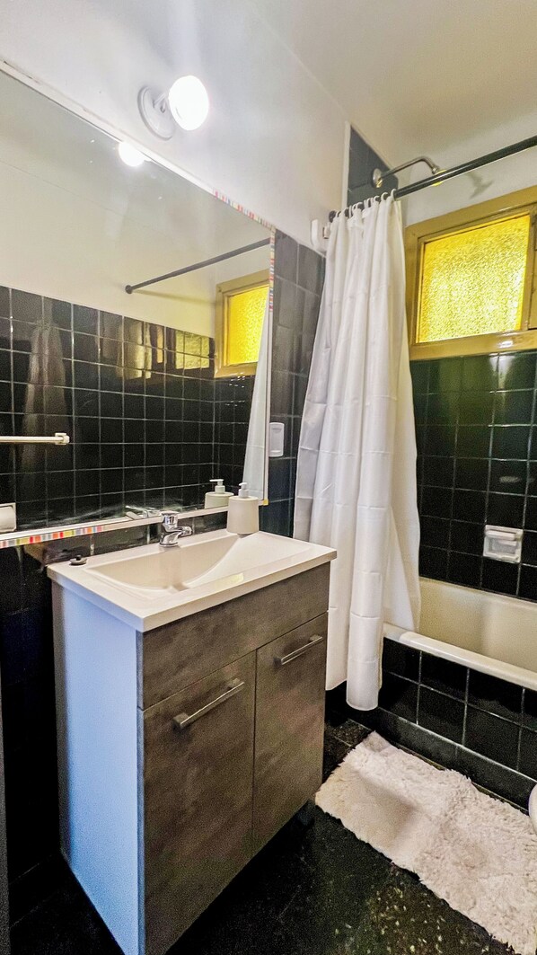 A bathroom with a white sink, dark tiled walls, a bathtub, and a shower curtain.