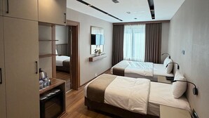 A modern hotel room with a wooden floor, a large wardrobe, a bed with a headboard, a bedside table, and a window with curtains. - GRAND SAVCILI DELUX (Gaziantep)