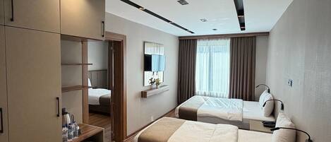 A modern hotel room with a wooden floor, a large wardrobe, a bed with a headboard, a bedside table, and a window with curtains.