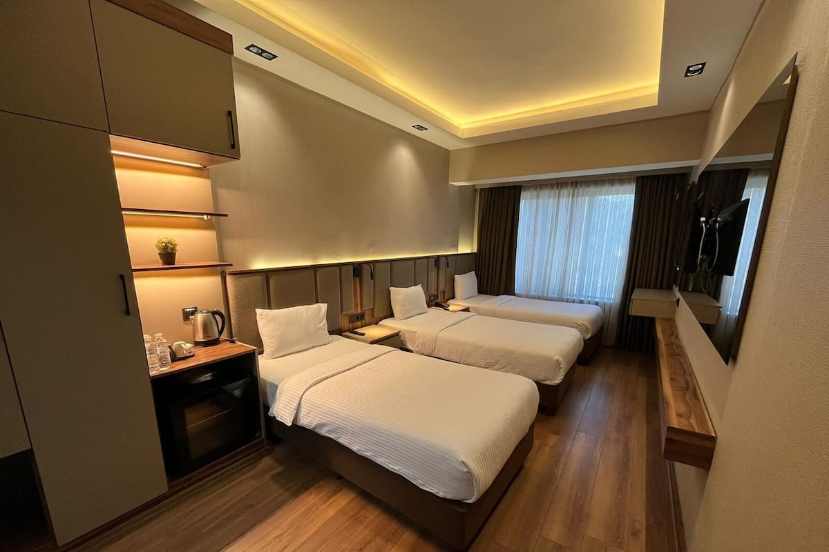 Ein Hotelzimmer mit zwei Betten, einem Schreibtisch mit Lampe, einer kleinen Pflanze und einem Fenster mit Vorhängen.