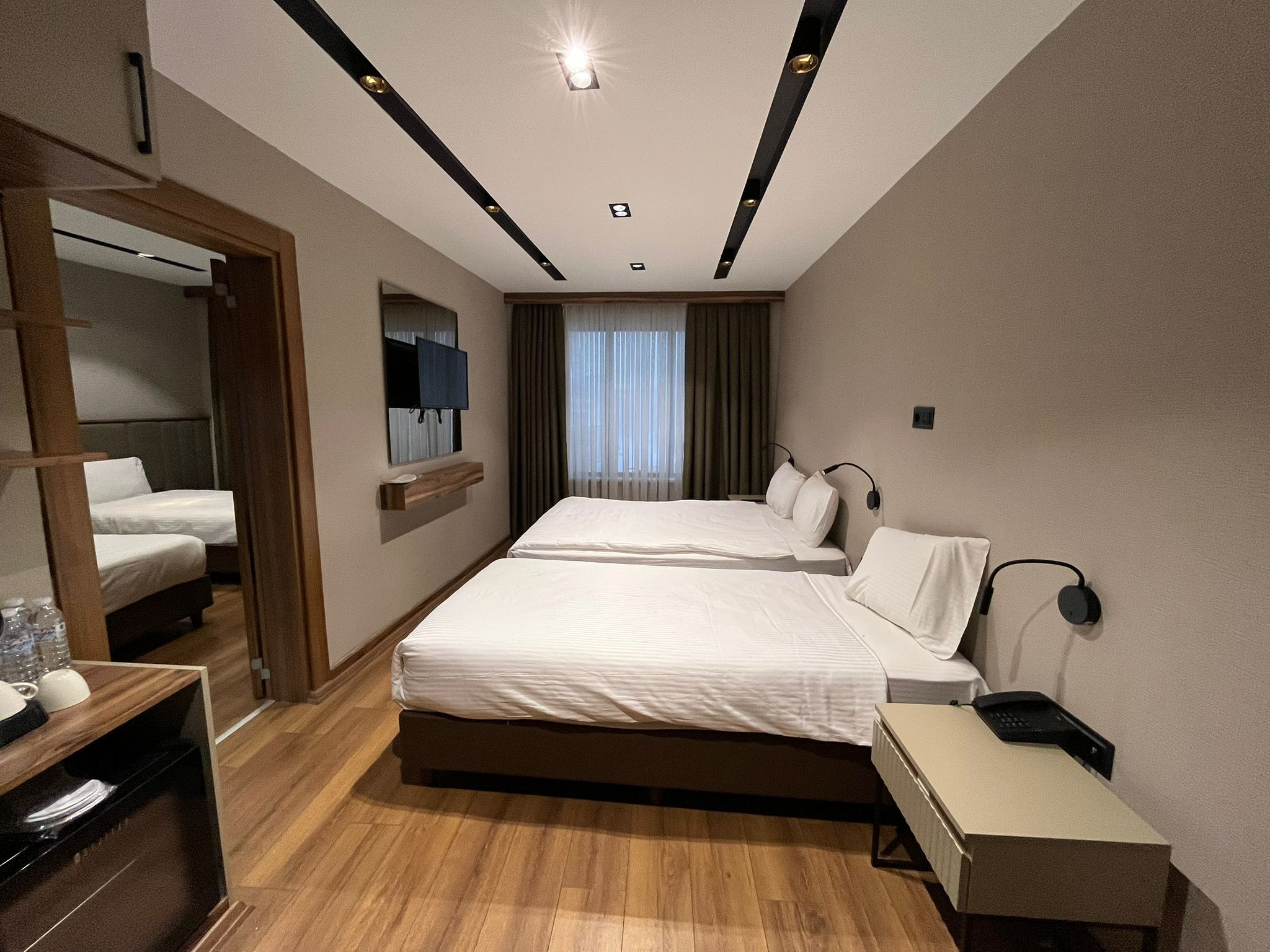 A hotel room with two beds, a desk with a telephone, a mirror, and a window with curtains.