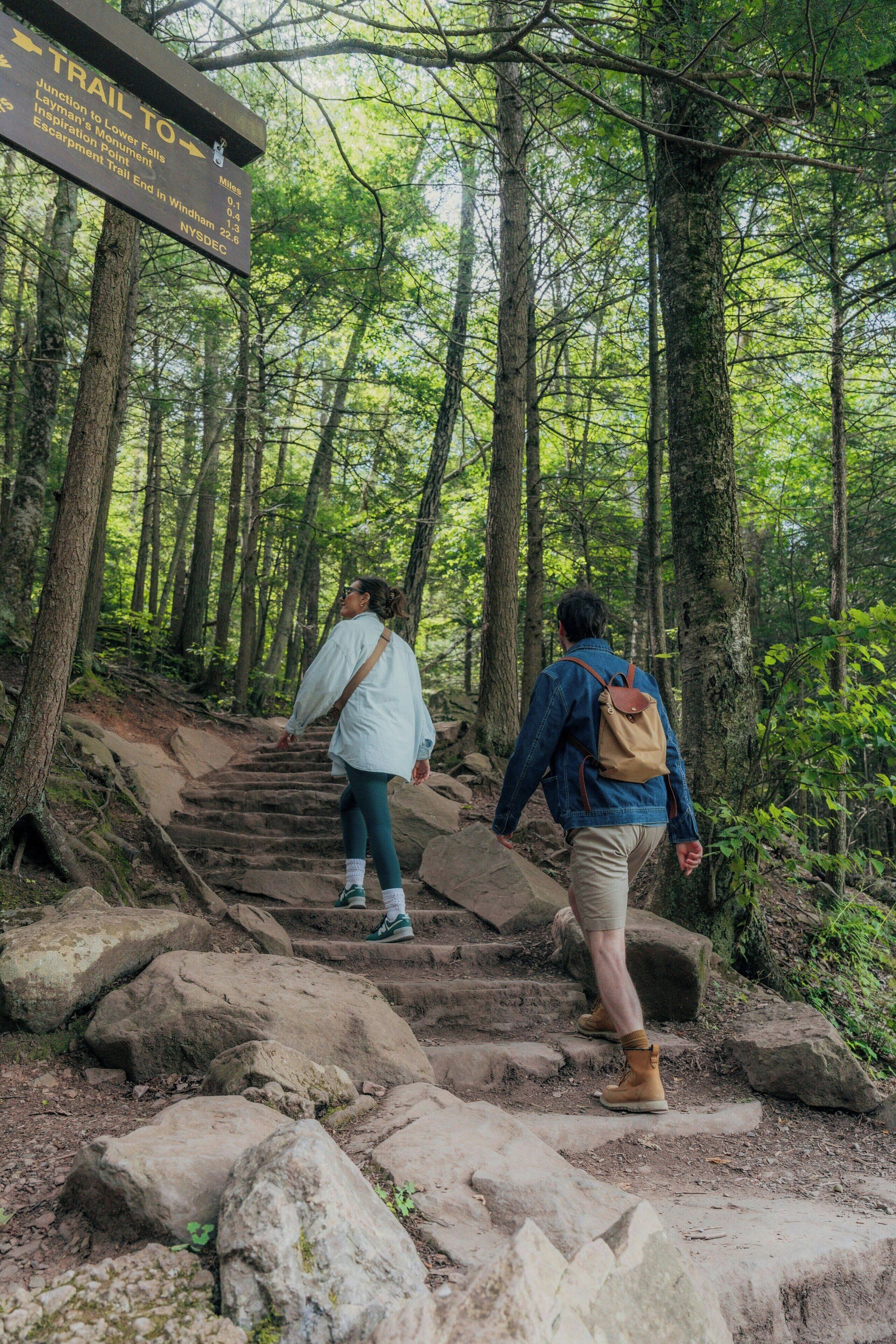 A trail sign in a forested area with a person ascending a rocky path.
