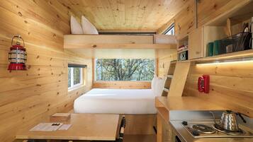 A compact cabin with a bunk bed, a small kitchenette, a table, and a window with a view of trees.