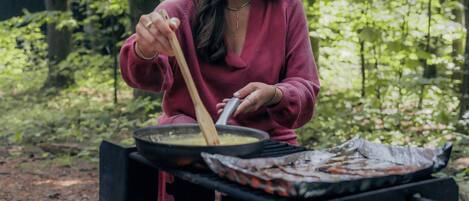A person cooking outdoors with a portable stove and a fire.
