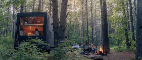 A forest cabin with a fire pit and people sitting outside.