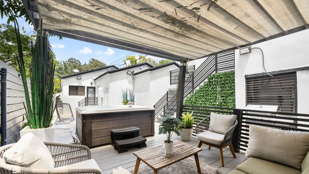Un patio exterior cubierto con mobiliario de mimbre, una mesa de madera y un jacuzzi.