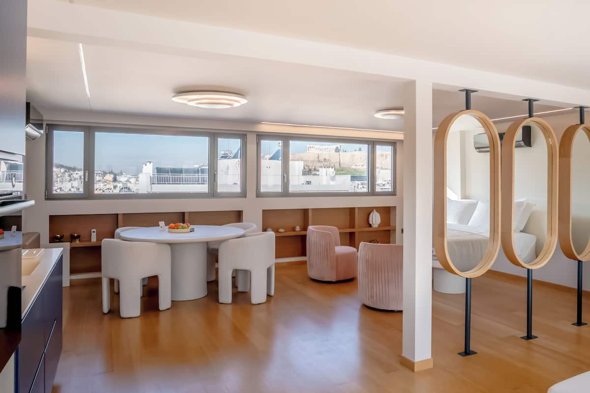 A modern hotel room with a dining area, large windows with city views, and a unique mirror installation.