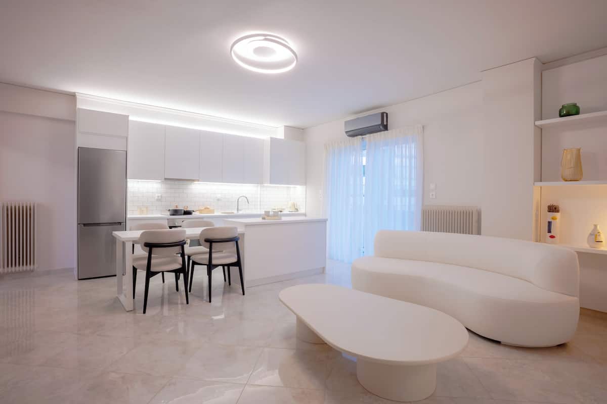 A modern kitchen with white cabinetry, a dining area with a white table and chairs, and a white sofa in a living area.