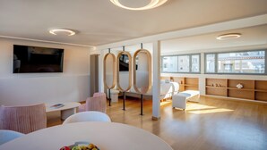 Quarto de hotel moderno com uma janela ampla, um espelho redondo, uma cama, uma mesa pequena e um banco.