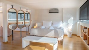 Quarto moderno com uma cama grande, mesas de cabeceira, um banco e uma televisão.