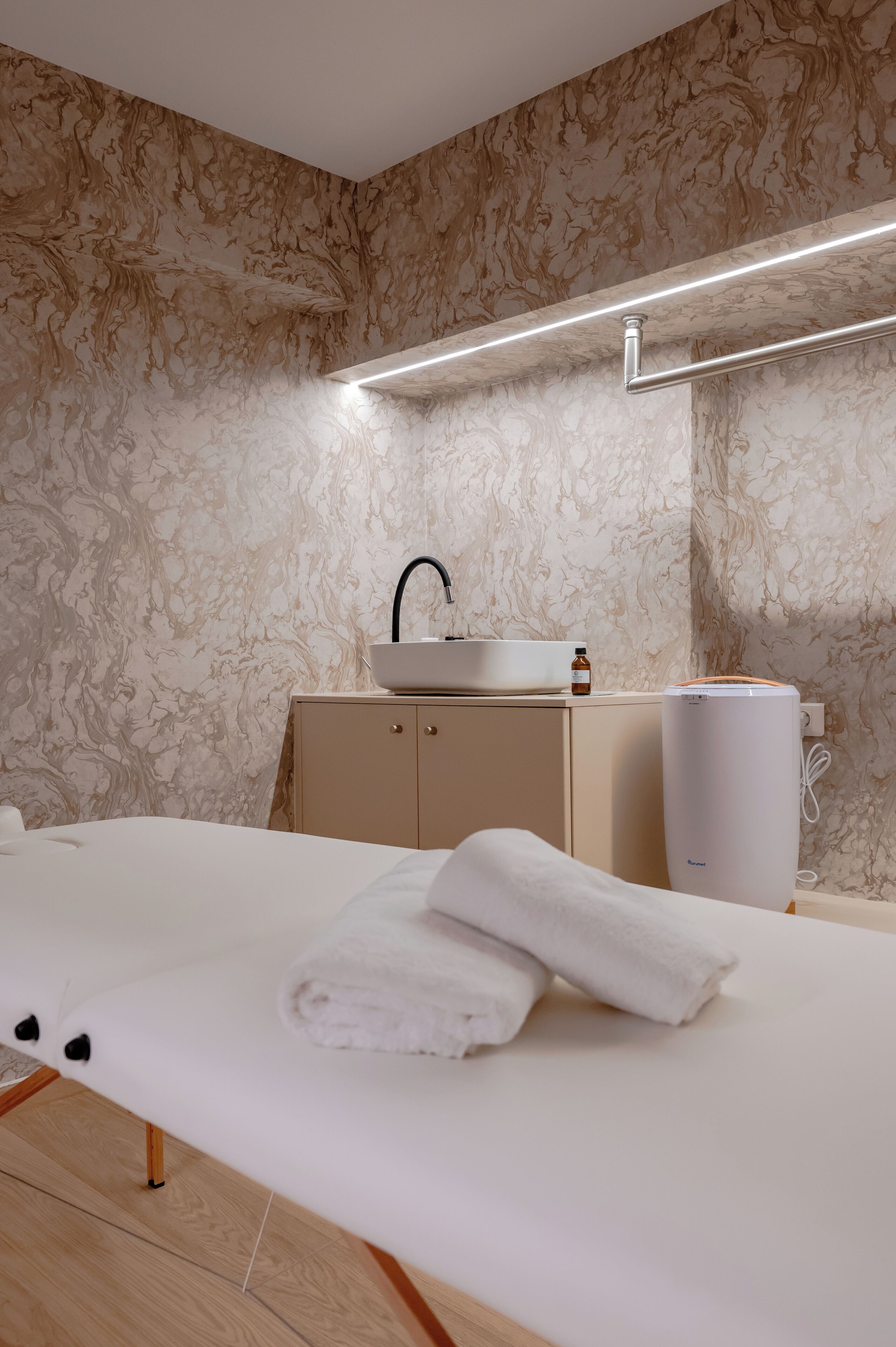 A modern bathroom with a marble-patterned wall, a white sink, a towel on the floor, and a white heater.