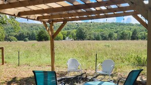 Une pergola en bois, avec une table et quatre chaises en dessous, installée dans un espace verdoyant offrant une vue sur un paysage boisé.
